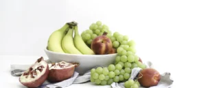 Frutero con plátanos, uvas, nectarinas y granada sobre fondo claro