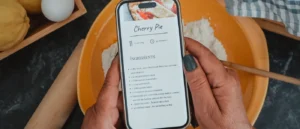Teléfono móvil mostrando una receta sobre una mesa con ingredientes de cocina
